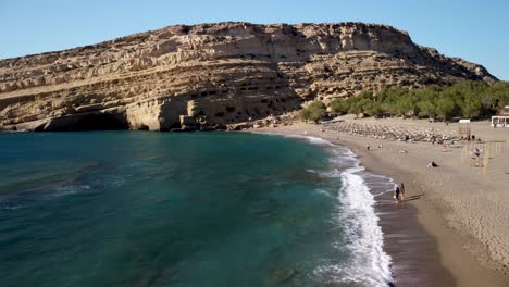 Drohnen-Dolley-Aufnahme-über-Dem-Strand-Von-Matala-Mit-Den-Matala-Höhlen-Im-Hintergrund