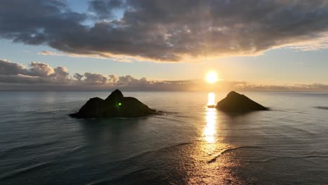 Hohe-Luftaufnahme-Der-Mokulua-Inseln-Bei-Sonnenaufgang-Mit-Sonne-Zwischen-Den-Inseln-Und-Ruhigem-Meer-Am-Morgen-Mit-Wolken-Am-Horizont