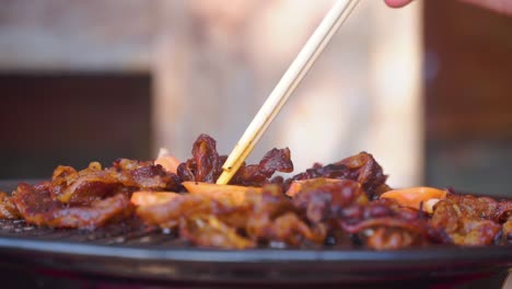 close up of hand using chopstick cooking japanese and korean bbq grill food