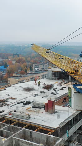 aerial view of construction site in the city. big crane and workers on the roof. construction of new apartment building in progress. vertical video