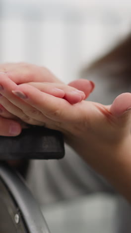 caring mother strokes hand of little daughter sitting in wheelchair on blurred background. woman shows care to schoolgirl with muscular dystrophy closeup