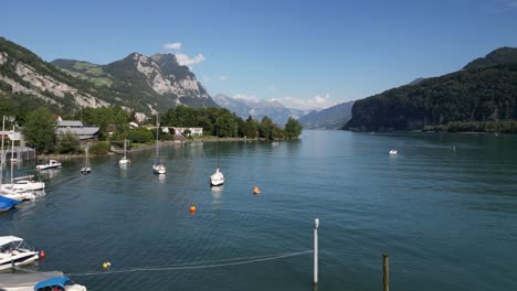 dock of different water vehicles boats and ships standing one of them moves forward to pass through the river that has on each sides massive hills mountains beach houses waves of water moving around