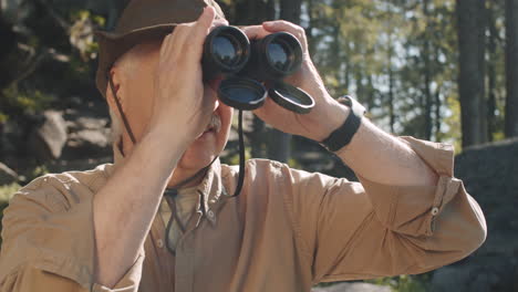 senior man hiking and using binoculars in the forest