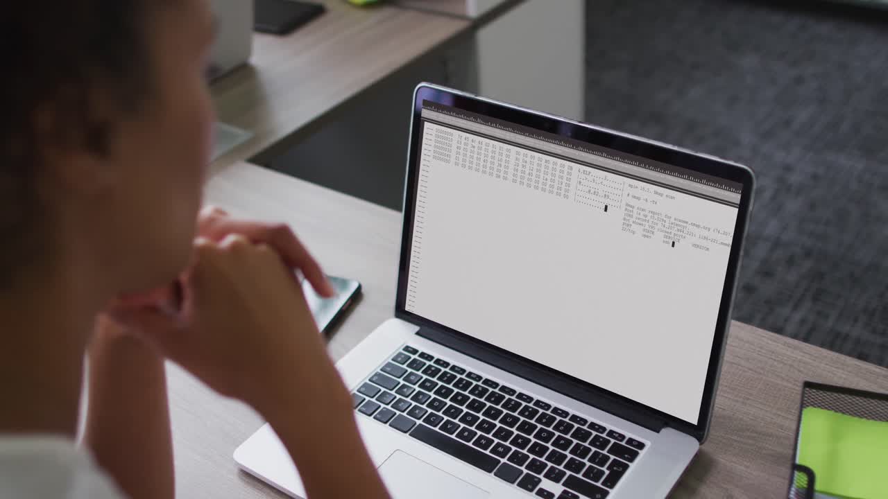 mujer de raza mixta sentada en un escritorio viendo el procesamiento de datos de codificación en la pantalla de un portátil
