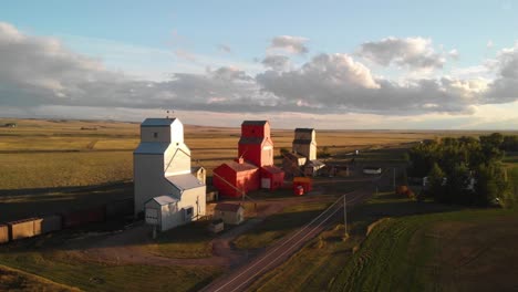 aerial rotating shot of three grain elevators surrounded by agricultural fields in southern alberta, canada at sunset