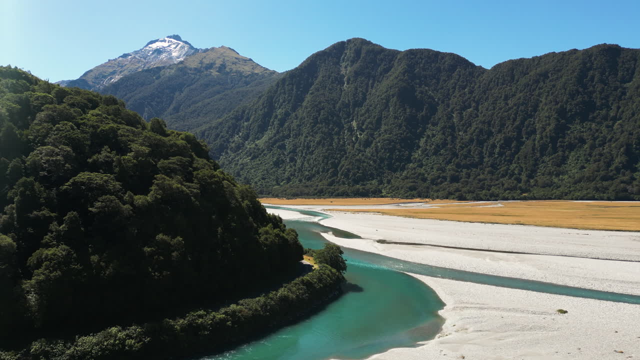 푸른 풀, 뉴질랜드에서 녹색 식물로 덮여 산맥으로 둘러싸인 맑은 녹색 좁은 강의 공중 무인 항공기 샷