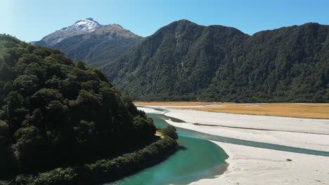 Aerial-drone-shot-of-clear-green-narrow-river-surrounded-by-mountain-range-covered-with-green-vegetation-in-Blue-Pools,-New-Zealand