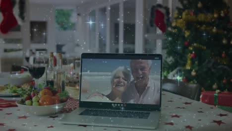 Animation-Von-Sternen-über-Dem-Weihnachtstisch-Und-Einem-älteren-Paar-Auf-Dem-Laptop-Bildschirm,-Das-Einen-Videoanruf-Tätigt