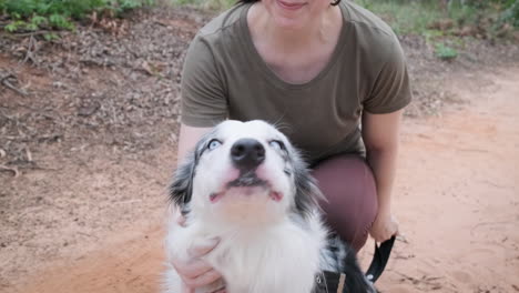 woman shows affection and trust to her australian shepherd dog, she holds him by his leash and caresses him