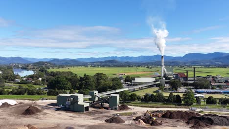 aerial footage of a sugar mill surrounded by lush fields and mountains under clear skies in murwillumbah, nsw