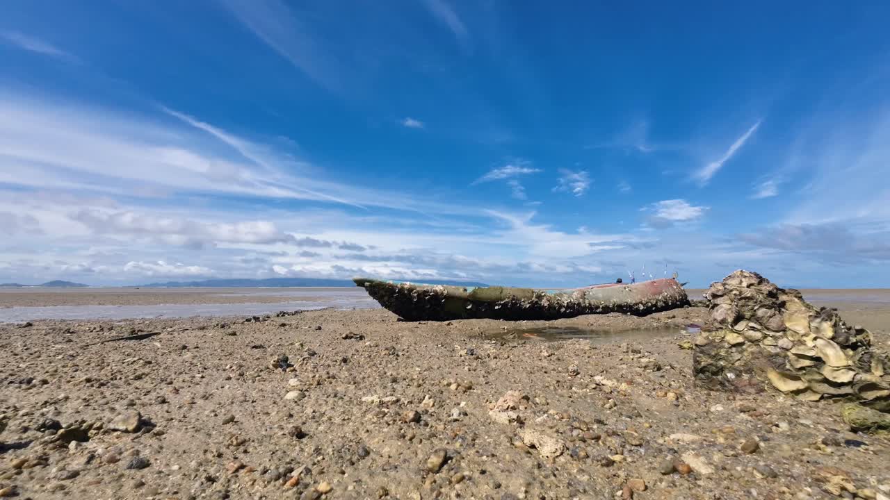 Timelapse footage of an old stranded kayak covered in seashells and algae on a sandy beach of Koh Phangan Thailand with moving clouds and scenic tropical seascape background