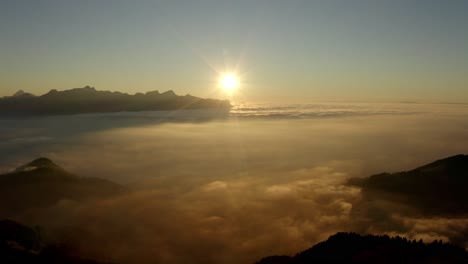 Descending-alongside-forest-hill-towards-sea-of-clouds-at-sunset,-the-Alps-in-the-background,-Switzerland