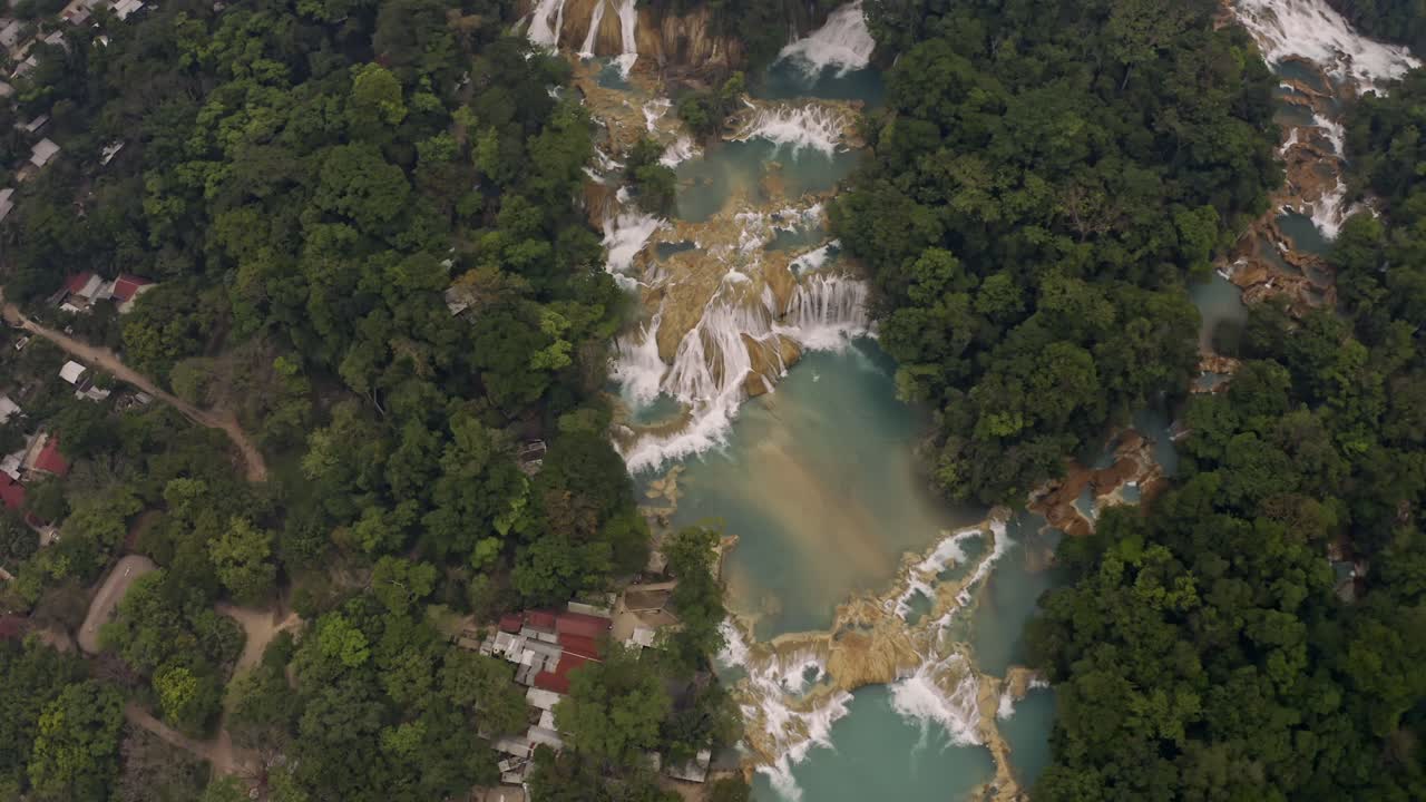 Aerial drone shot of the Agua Azul waterfalls in Chiapas, Mexico. The perspective shows the stunning turquoise water cascading over limestone formations