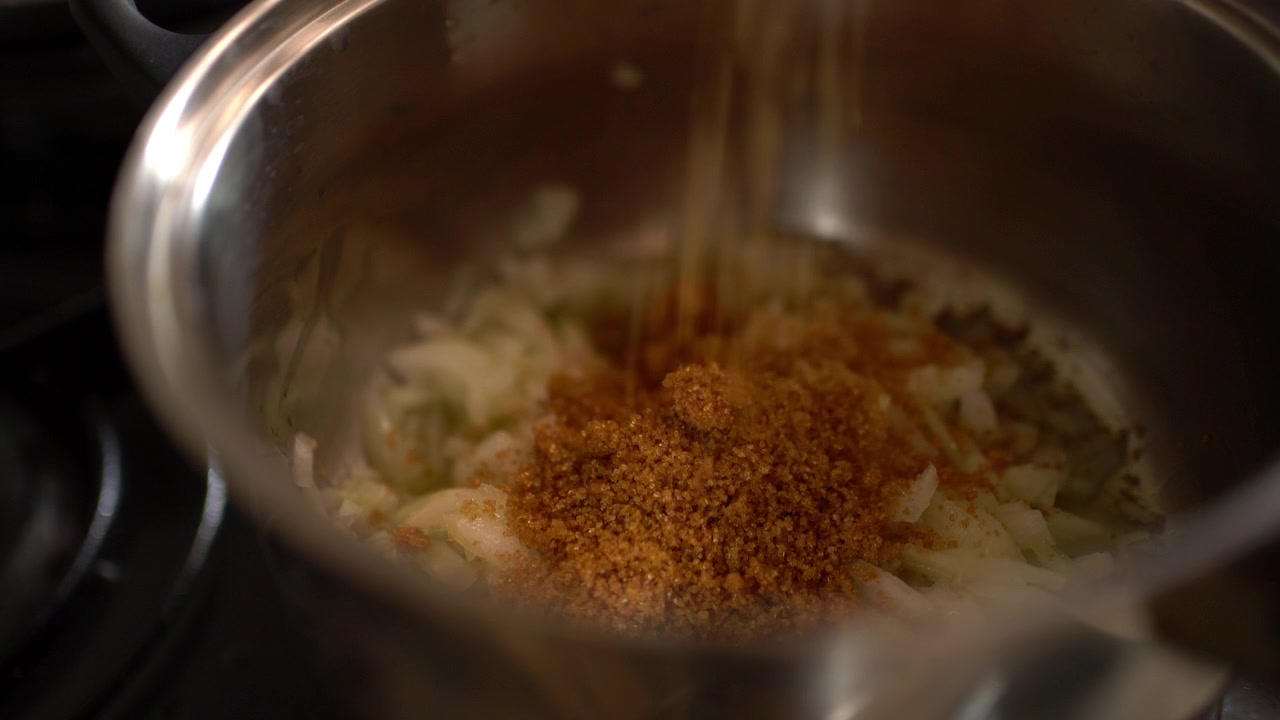 Una padella di cipolle cuoce lentamente in olio d'oliva mentre viene aggiunto zucchero di canna, un passaggio prima di preparare la salsa di pomodoro