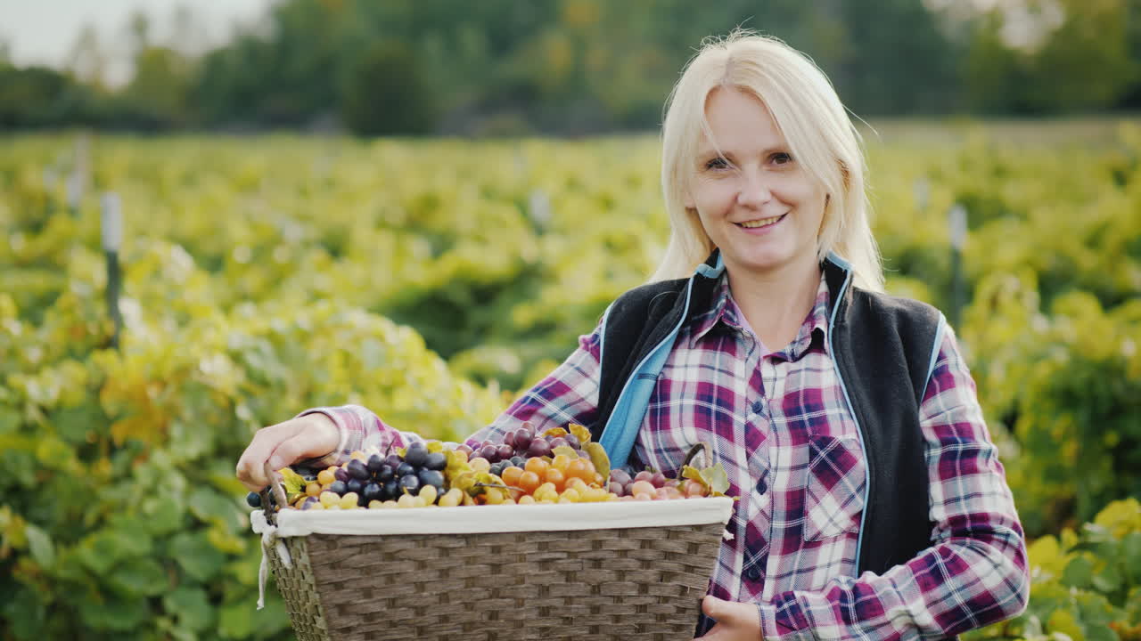 포도 미소가 담긴 바구니를 든 매력적인 농부의 초상화가 카메라를 쳐다본다