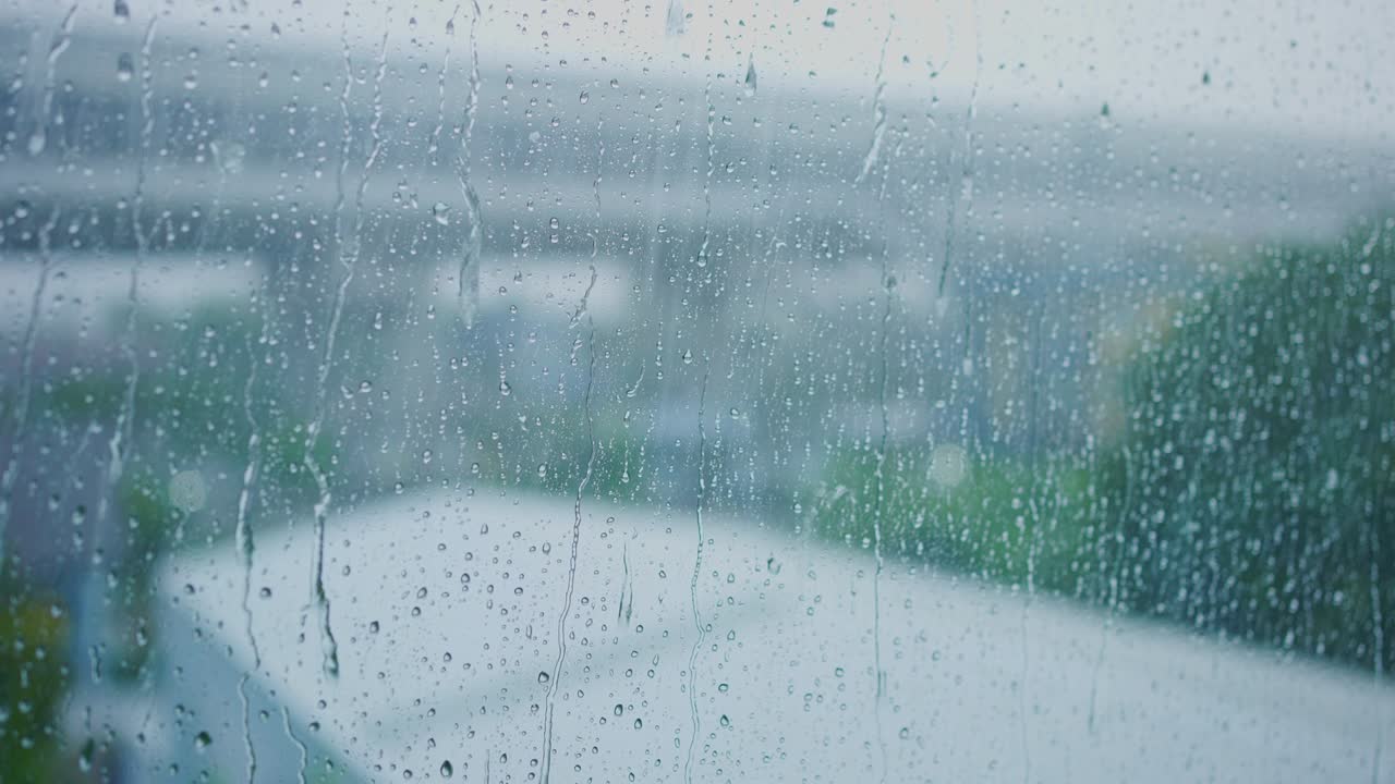 비가 오는 계절을 위한 녹색 공원 배경으로 창문 유리 위에 물이 떨어지는 느린 동작 장면