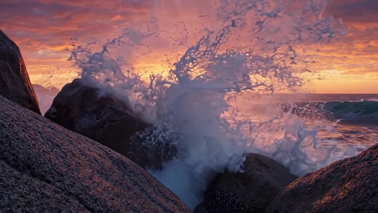 Breathtaking Sunset Over the Ocean, Captured Between Majestic Rocks at the Shoreline, Illuminating the Sky with Vibrant Colors and Reflecting on the Waves