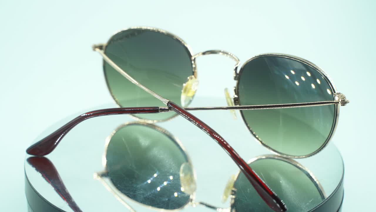 360도 회전하는 스탠드에 금색 선글라스를 놓는 클로즈업 영화 샷, 그을린 유리, 스튜디오 조명, 제품 4k 비디오, 느린 동작