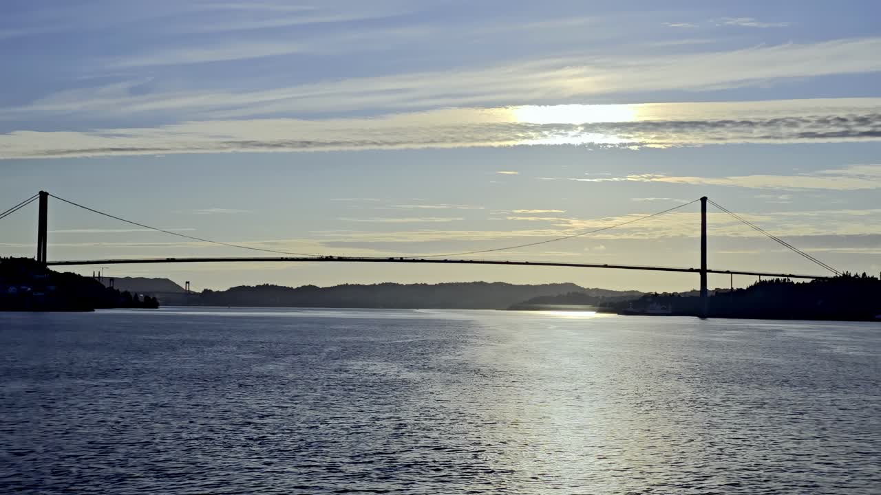 Boat nears Askoy Bridge from sea as the structure appears in silhouette against golden sunset light
