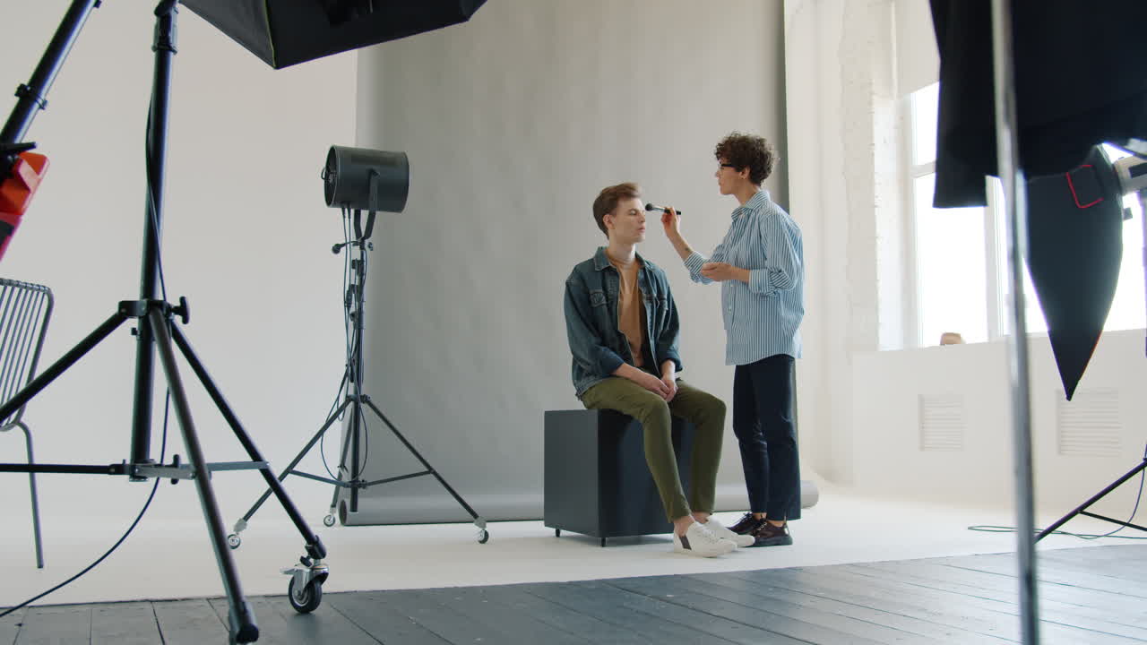 artista de maquillaje aplicando maquillaje a un modelo en un estudio fotográfico