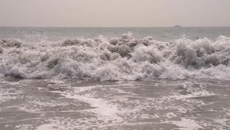 Cerca-De-Las-Olas-Del-Océano-Pacífico-Chocando-Contra-La-Playa-De-Arena-En-Cámara-Lenta-En-San-Diego,-California,-Con-Un-Gran-Barco-En-El-Fondo