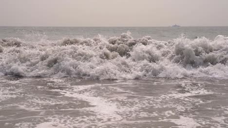 cerca de las olas del océano pacífico chocando contra la playa de arena en cámara lenta en san diego, california, con un gran barco en el fondo