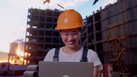 close up de una trabajadora asiática que usa gafas de protección y casco de seguridad usando una computadora portátil mientras está de pie en un sitio de construcción