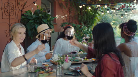 Amigos-Haciendo-Tostadas-Celebrando-Una-Cena-Bebiendo-Vino-Comiendo-Comida-Mediterránea-Sentados-En-La-Mesa-Disfrutando-De-Un-Hermoso-Día-De-Verano-Al-Aire-Libre-Imágenes-De-4k