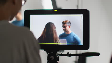 female film director watching male and female actors holding scripts rehearsing for shooting movie or video in studio on monitor