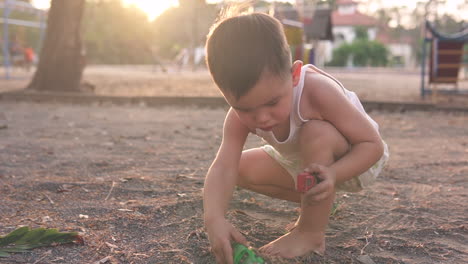 video en cámara lenta de un lindo niño asiático felizmente jugando solo con autos de juguete y suciedad en un parque infantil al aire libre al atardecer con hermosa luz de fondo