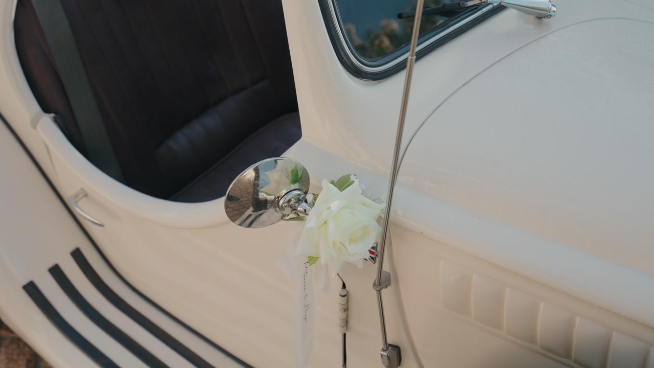 Close up of a vintage wedding car with a white rose decoration tied to the side mirror