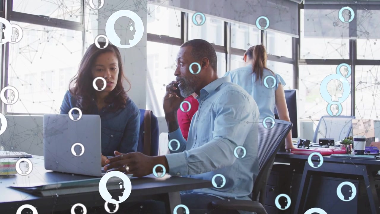 Man taking call pointing at laptop, peer working business update, animated icons drifting over desk