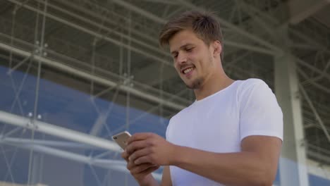 un hombre guapo sonriente caminando con un teléfono inteligente en la calle.