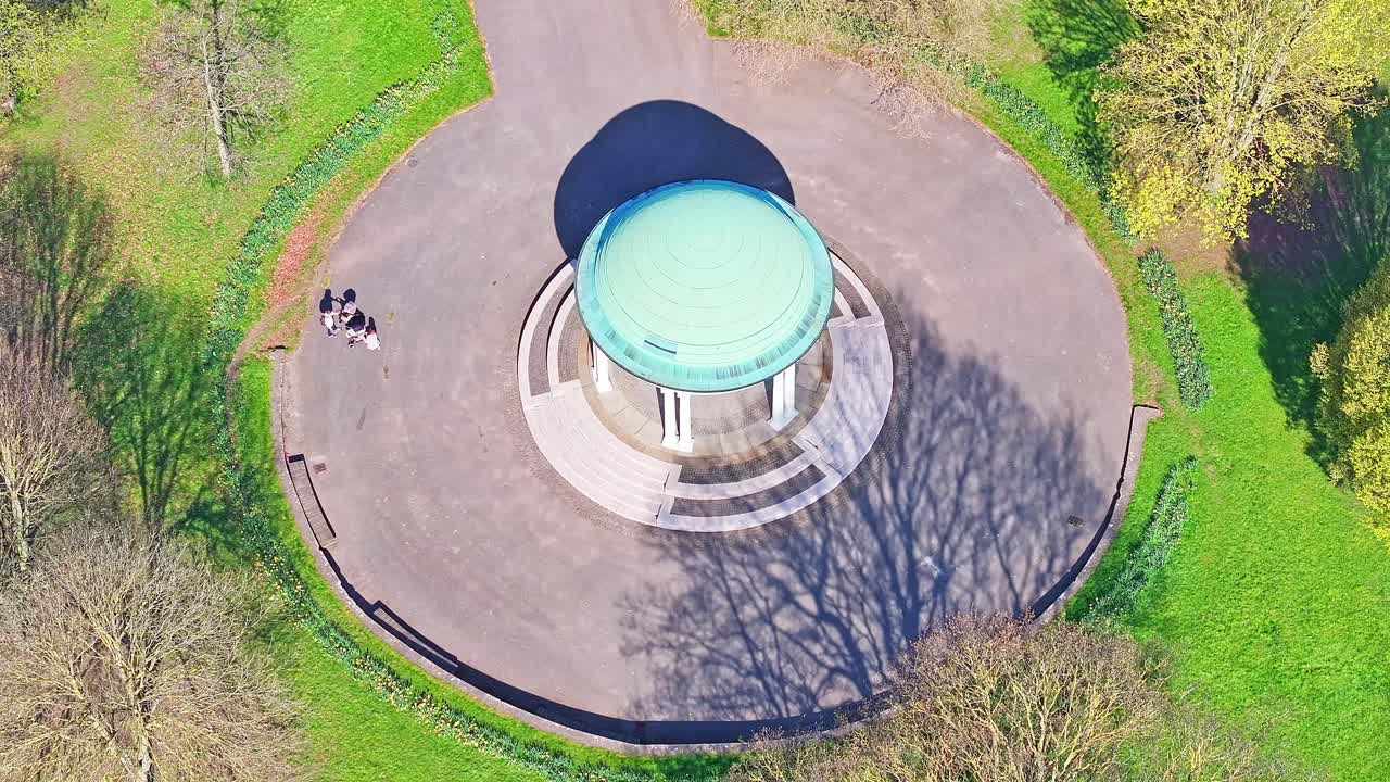 Straight down aerial of circular gazebo at center of lawn feature within large green parkland, Clifton Park UK