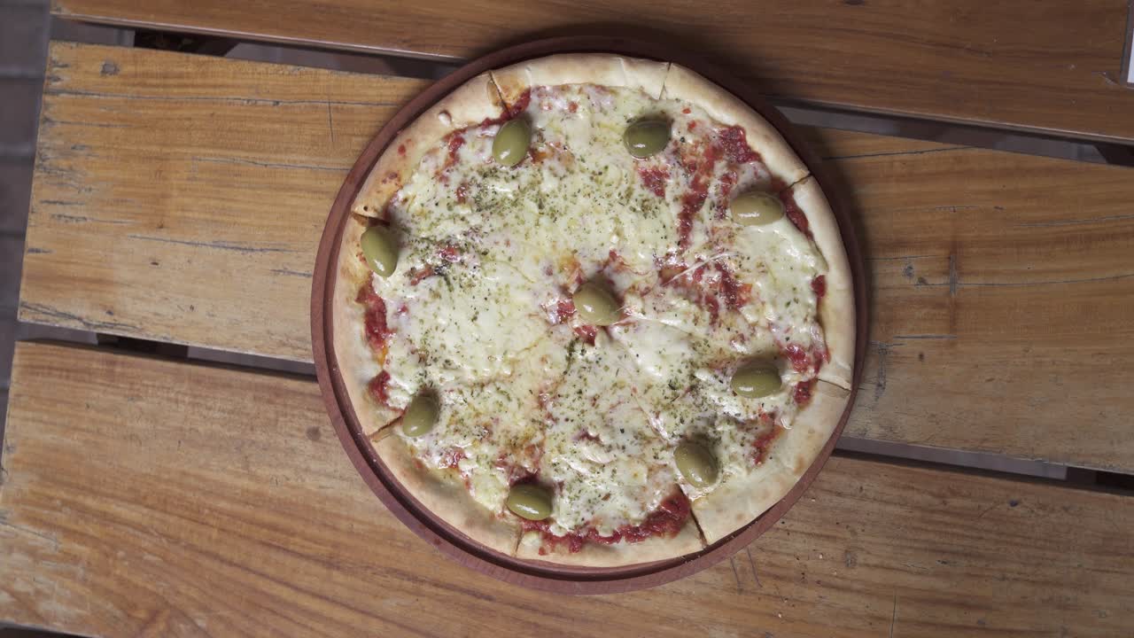 Pizza Margherita che gira con formaggio e olive su tavolo di legno, primo piano dall'alto