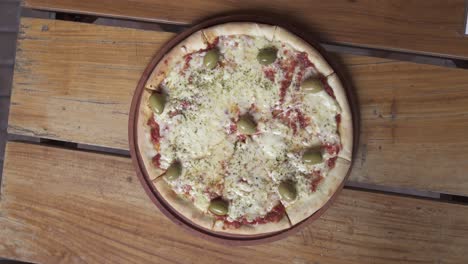 rotating margarita pizza with cheese and olives on wooden table,close up top down