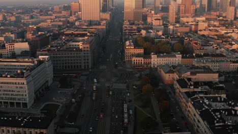 Slide-and-pan-aerial-footage-of-roundabout.-High-rise-office-tower-illuminated-by-bright-rising-sun-in-background.-Warsaw,-Poland