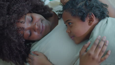 african american mother and child cuddling and talking on bed