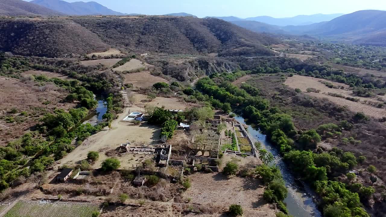 Bird’s eye view of Ex Hacienda San Jacinto Ixtoluca ruins, La Mezquitera, Morelos, located near a river, surrounded by fields, trees, and mountains. Backward panoramic flight