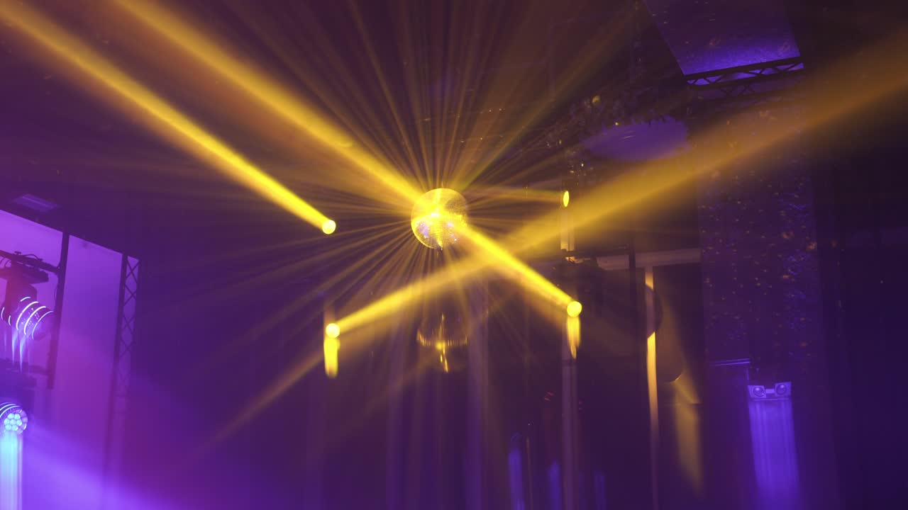 Golden light rays shine from a disco ball, creating a radiant glow in a colorful event setting