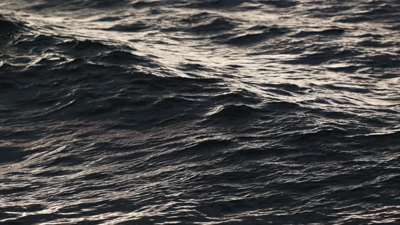 Following waves crashing into rocks at sunset in slow motion close up and moody