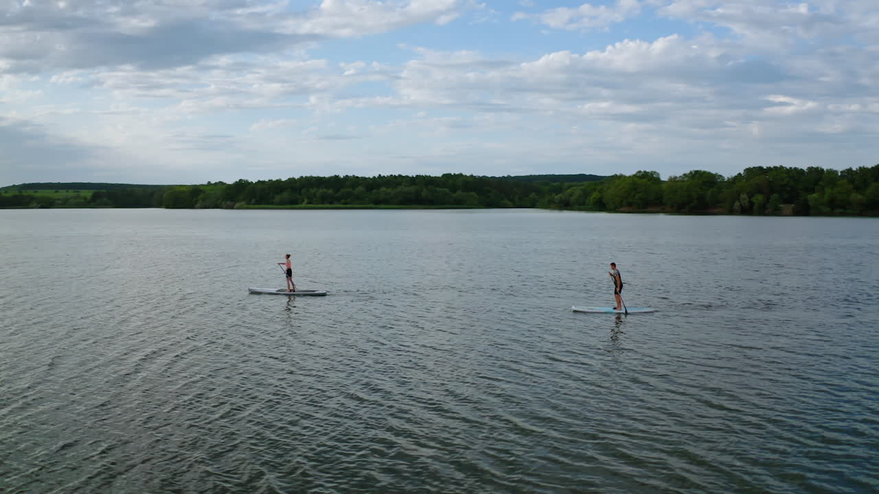 Young people doing water sport in the evening. Active friends swimming along a river standing on a boat with oars. Healthy lifestyle. View from above.