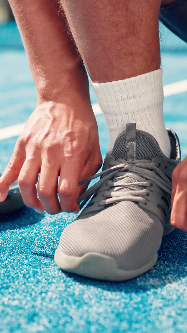 Primo piano di mani che allacciano i lacci delle scarpe su un campo sportivo blu