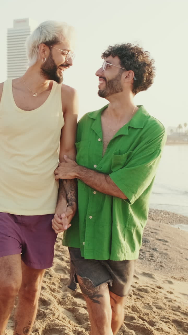 Coppia gay felice che passeggia mano nella mano su una spiaggia assolata