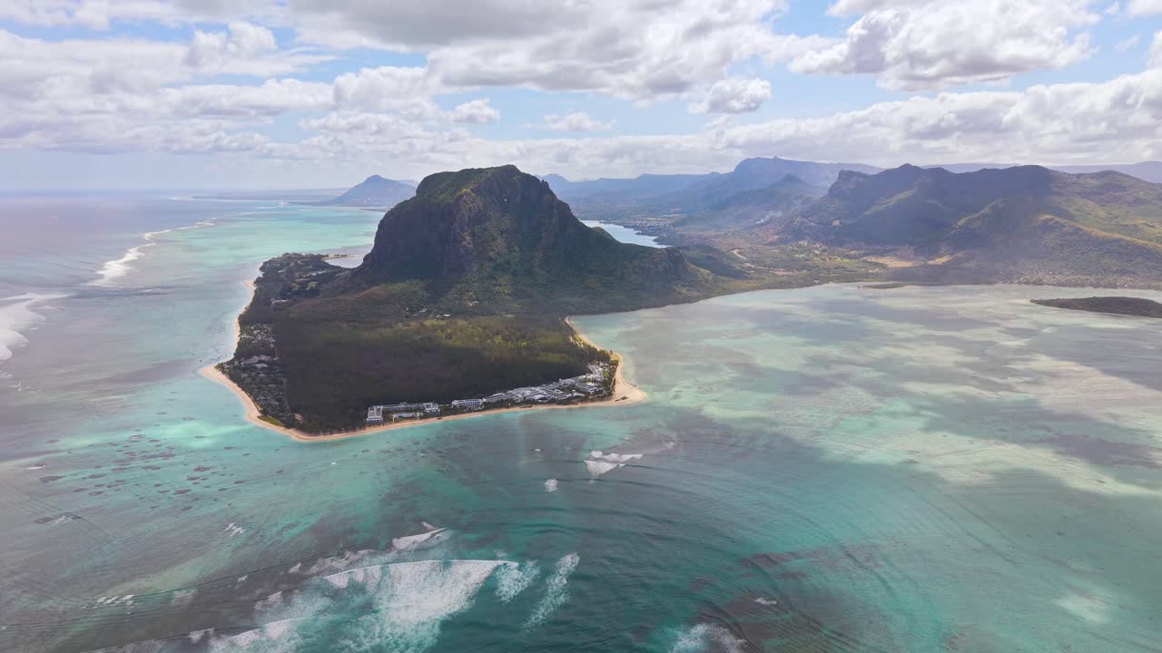 Aerial view of Le Morne Brabant and the famous underwater waterfall illusion in Mauritius, surrounded by turquoise waters, coral reefs, and tropical scenery under bright clouds