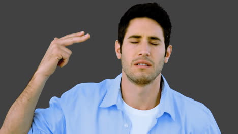 Man-pretending-to-shoot-himself-with-hand-on-grey-background