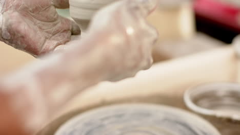 Hands-of-african-american-female-potter-holding-clay-jug-in-pottery-studio,-slow-motion