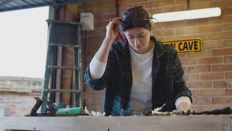 young female carpenter drawing and measuring woodwork design in garage workshop