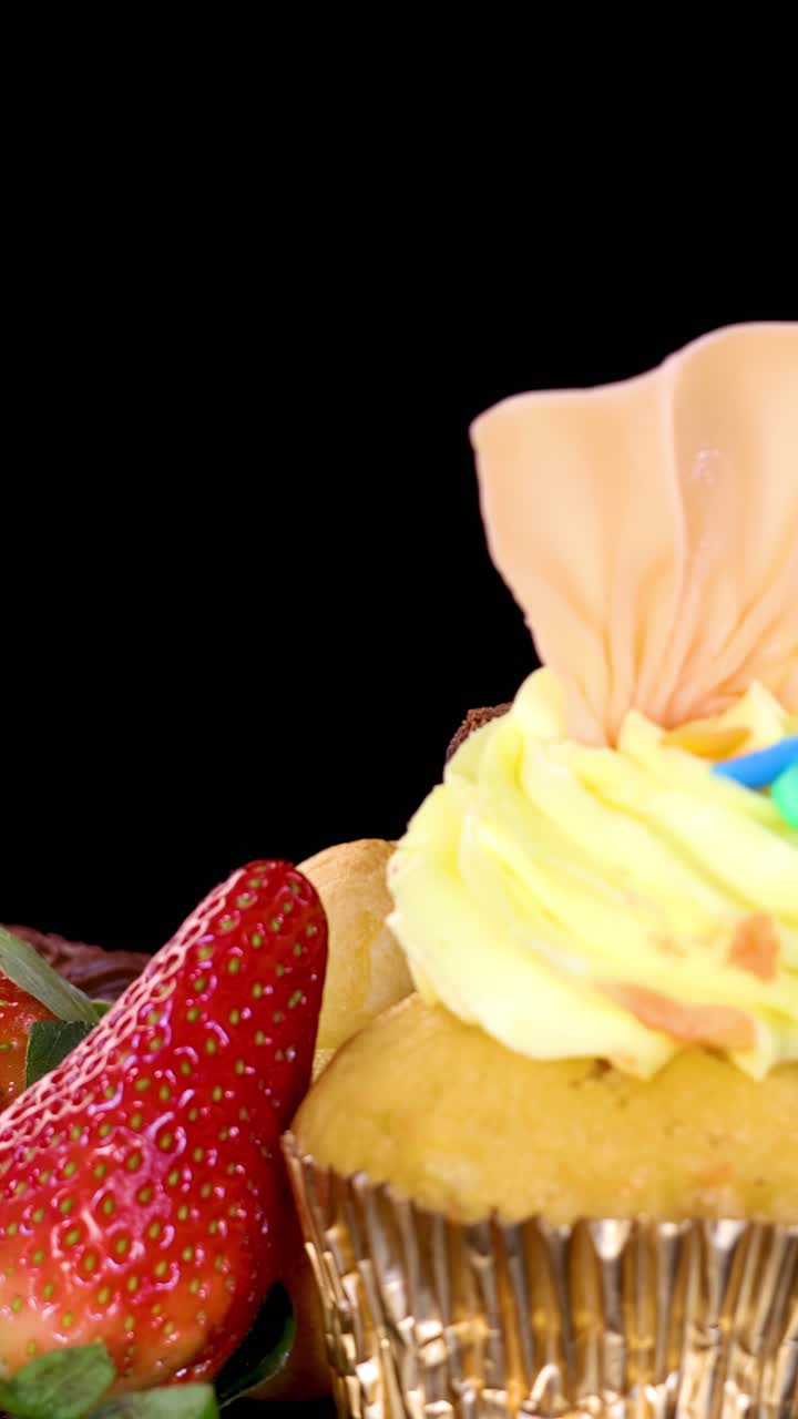 Una fluida carrellata in primo piano rivela cupcake, dessert al cioccolato, fragole e pasticcini su uno sfondo nero con un'illuminazione brillante e uniforme e colori vivaci.