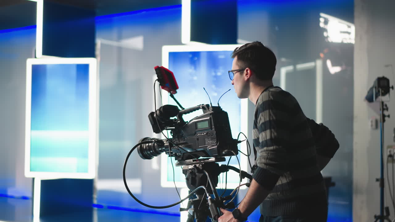 Camera operator adjusting professional video camera in studio with high-tech lighting setup. Filming process for broadcast production in modern studio environment with equipment and cable